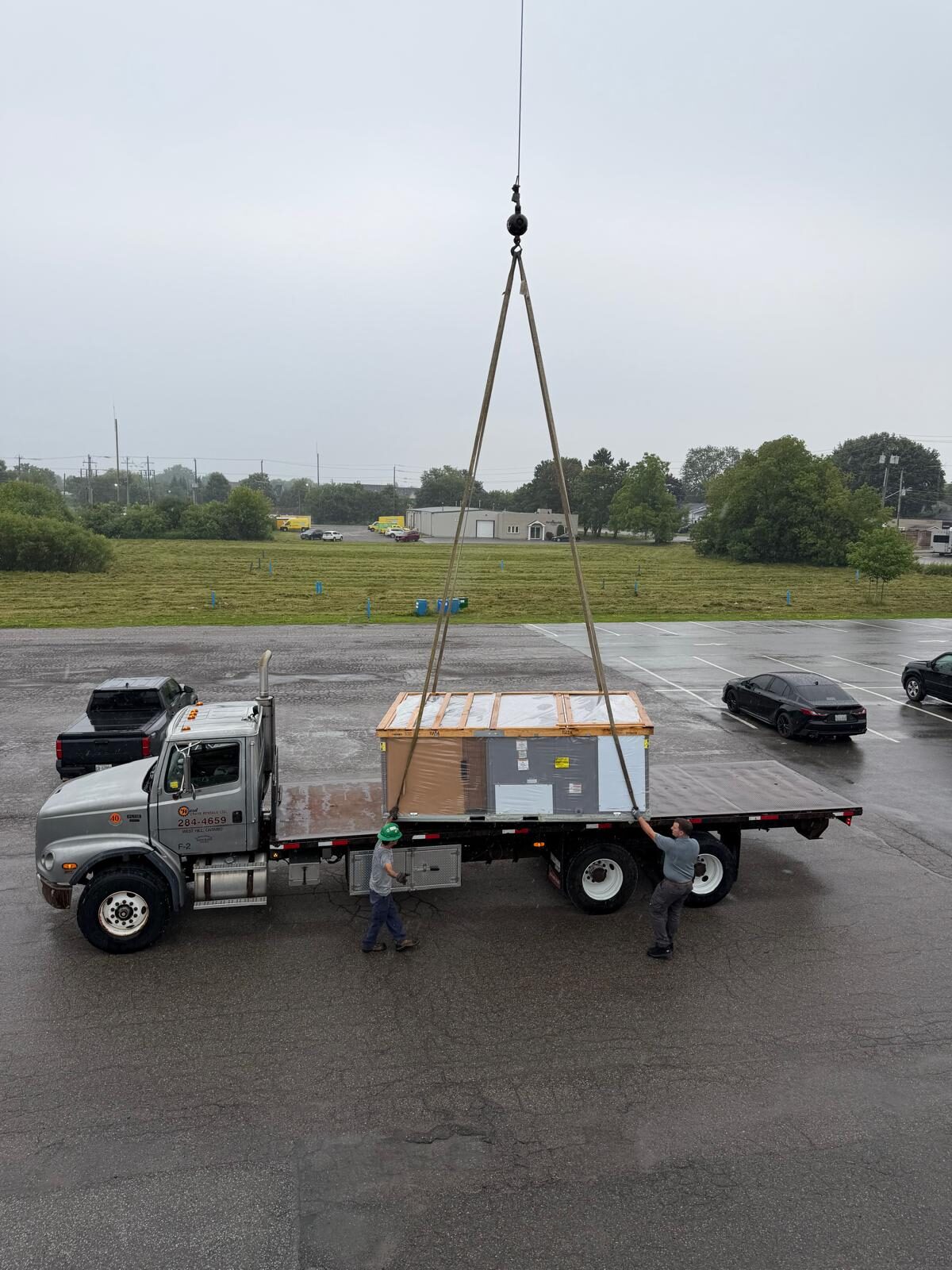 Crane lifting a packaged rooftop unit from a flatbed truck